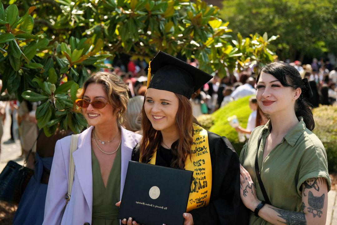 Graduate poses with family and friends outside of Reed Green Coloseum 