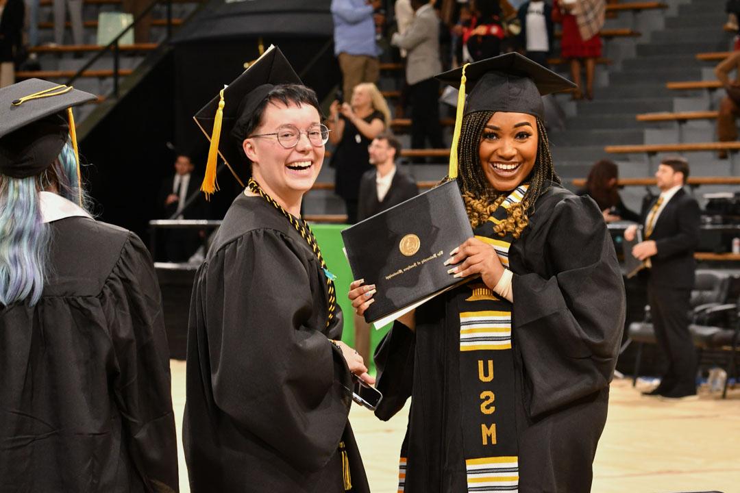 Students smile with their diplomas at commencement. 